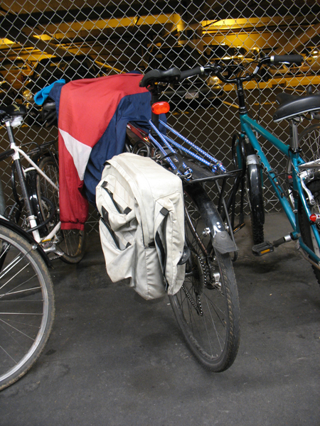 A rear rack on a bicycle with a pannier.  This bike also has bungee cords on the rack, which help strap items down.