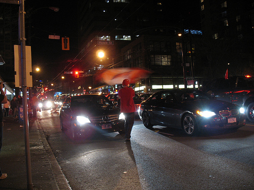 A fellow waving a flag in front of a car in the street.