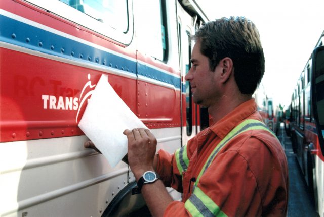 An employee installs the TransLink logo on the side of this bus after scraping off the BC Transit logo.