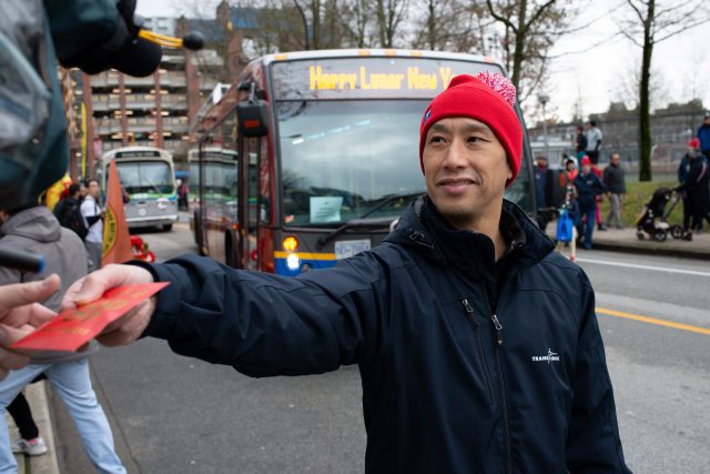 Man handing out red envelope with TransLink bus at Lunar New Year Parade 