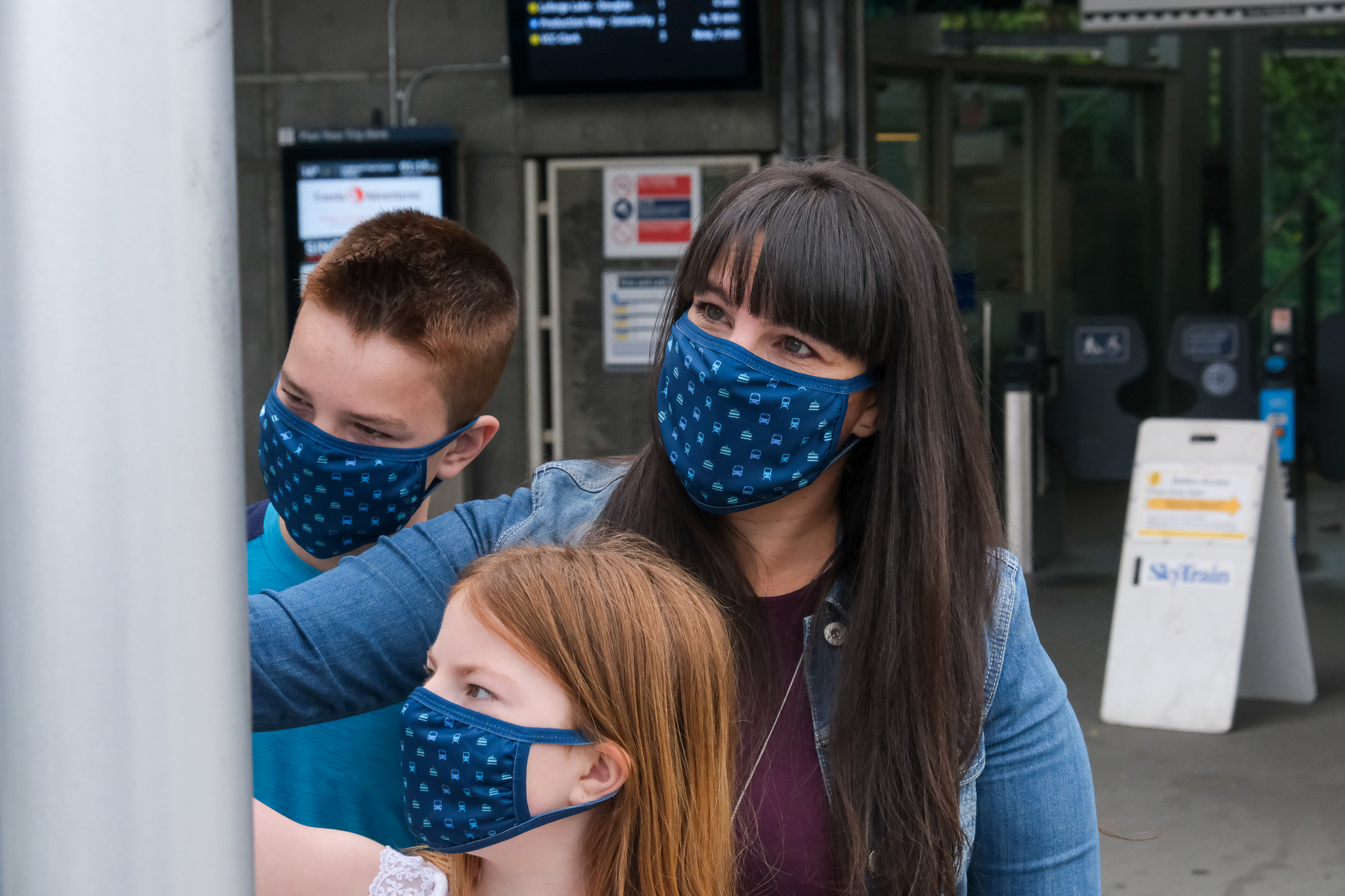 A mom and two children wearing masks looking at a transit map