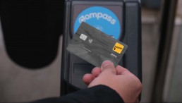 Photo of a hand holding up an interac debit card at a SkyTrain fare gate