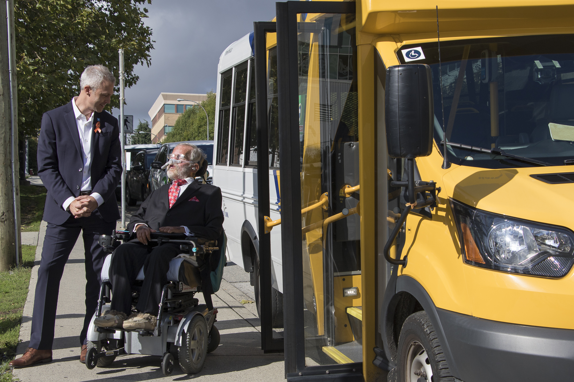 TransLink CEO Kevin Quinn and chair of TransLink HandyDART User Advisory Committee Tim Louis who is in a wheelchair are seen beside a HandyDART shuttle with its doors open 