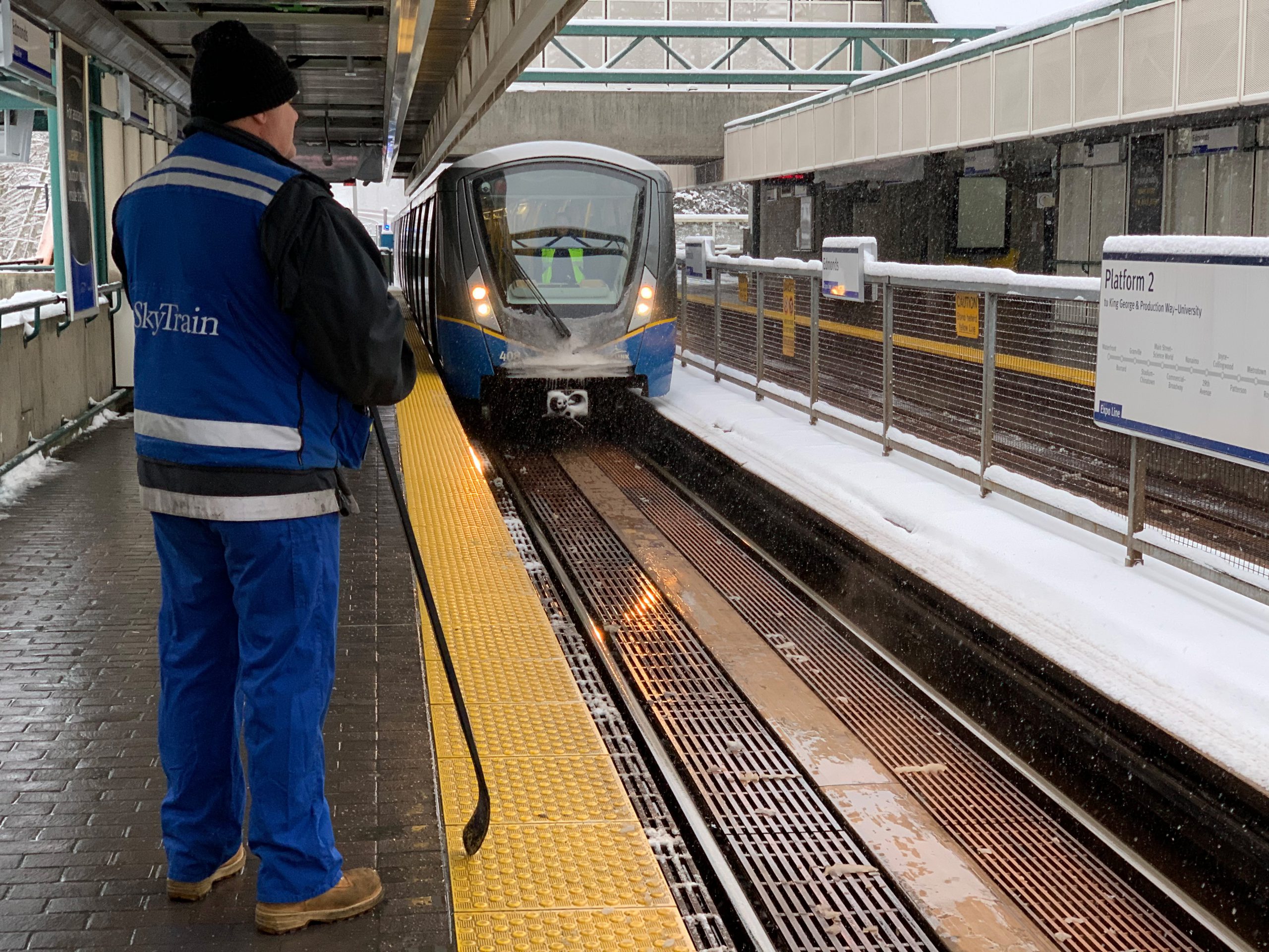 A SkyTrain technician prepares to clear snow and ice from the doors of the arriving SkyTrain car