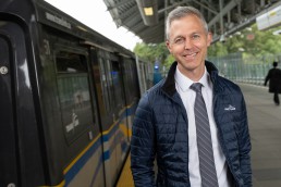 TransLink CEO Kevin Quinn stands on a SkyTrain platform with a SkyTrain passing in the background