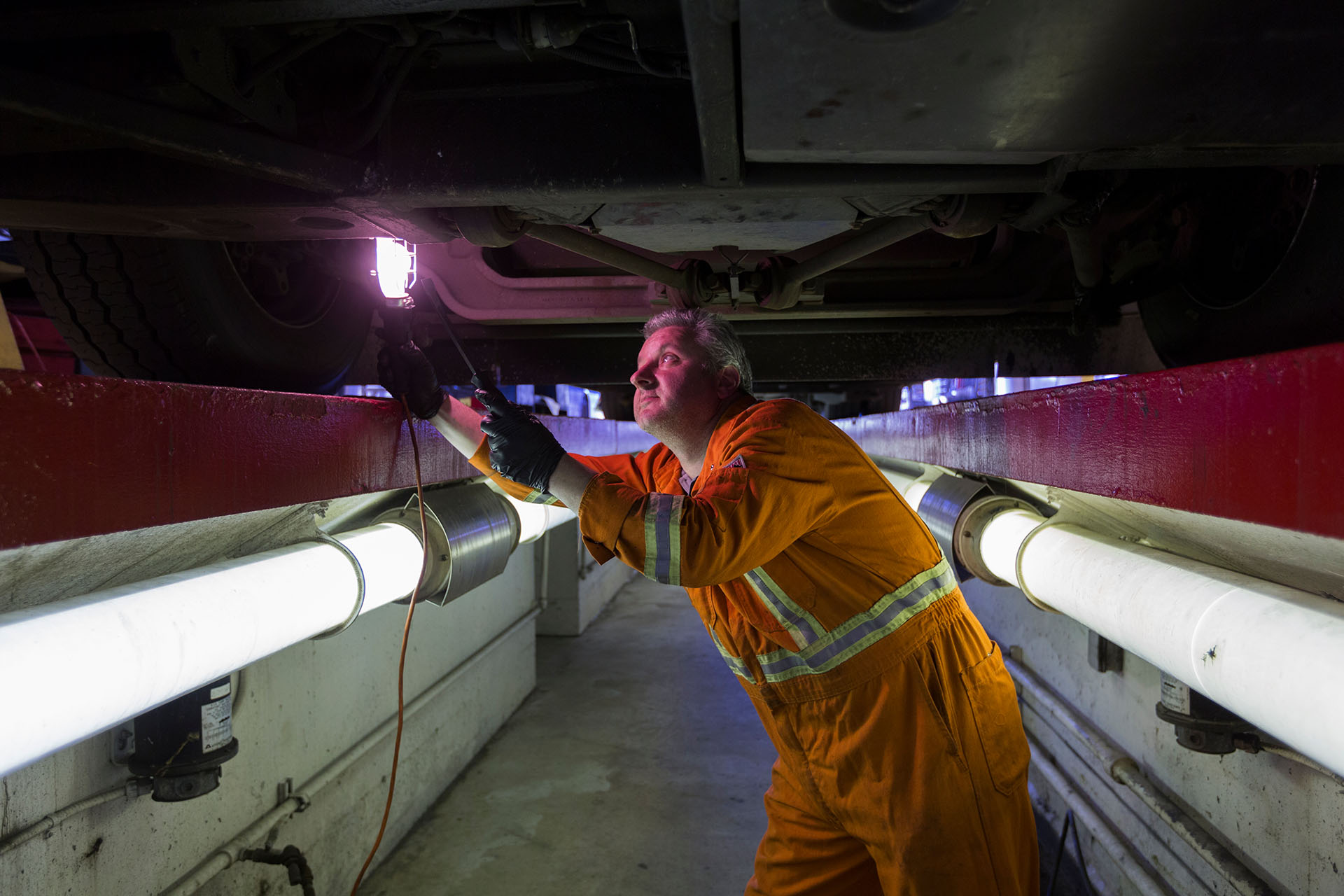 A mechanic examines underneath a bus with a light
