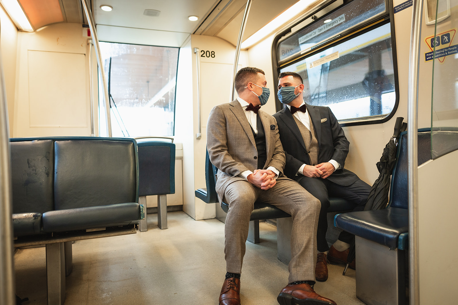 Two grooms seated side by side on SkyTrain gazing into each others eyes