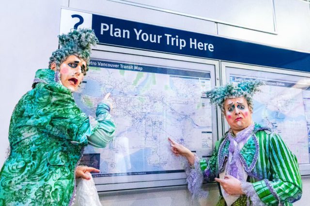 Two Cirque du Soleil clowns in costume posing in front of transit map SkyTrain station. 