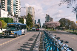 Route 23 bus traveling on Beach Avenue in Vancouver with bike racks in foreground and buildings and trees in background.