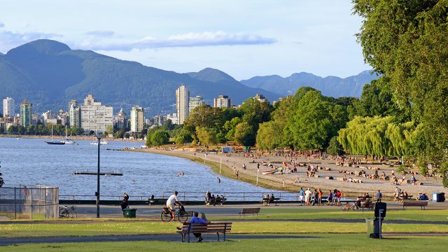 A wide view of Kitsilano beach and the Vancouver skyline and people relaxing by the sea