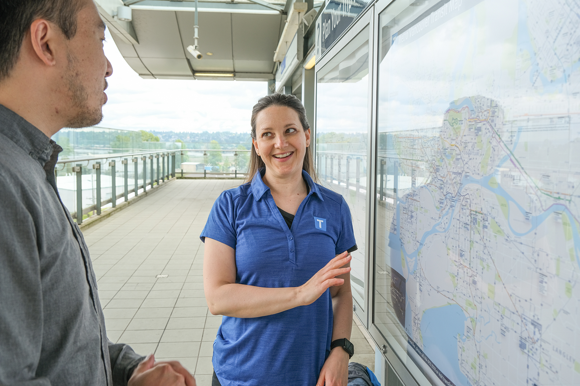 TransLink volunteer interacting with transit customer in front of transit system map.