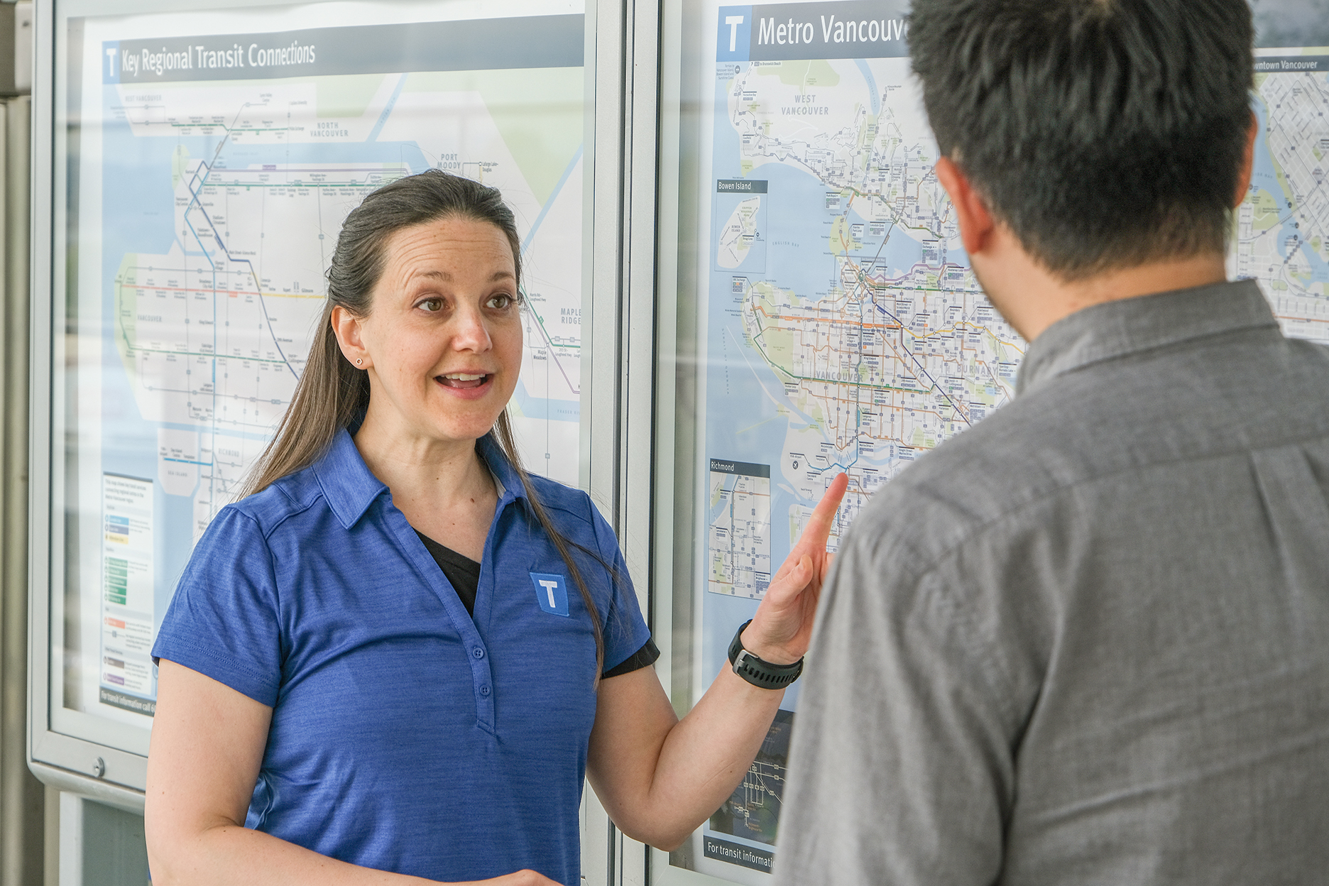 A TransLink volunteer helps a transit customer while pointing at transit system map.