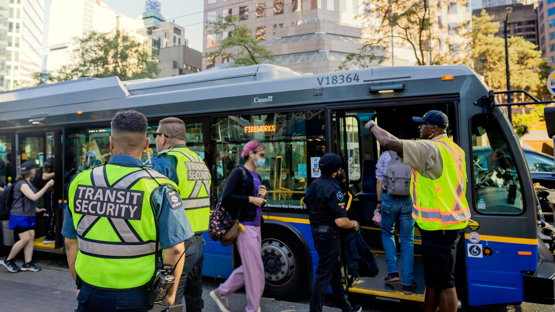 Transit employees wearing high-vis vests direct people aboard a bus that reads "Fireworks"