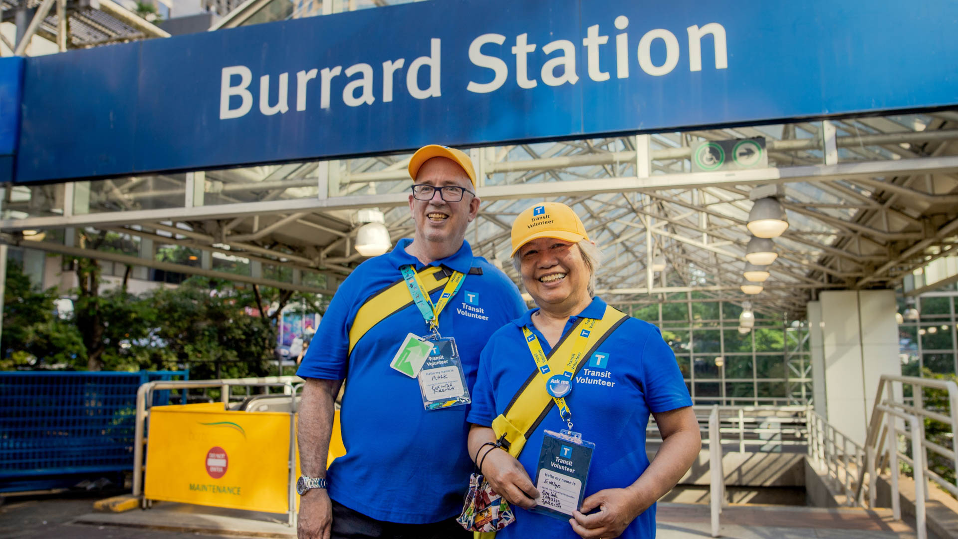 TransLink Volunteers Mark and Evelyn are dressed in blue and yellow branded-gear and pose outside of Burrard Street Station for a photo