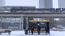 Commuters waiting at a bus stop while SkyTrain passes by at Metrotown Station