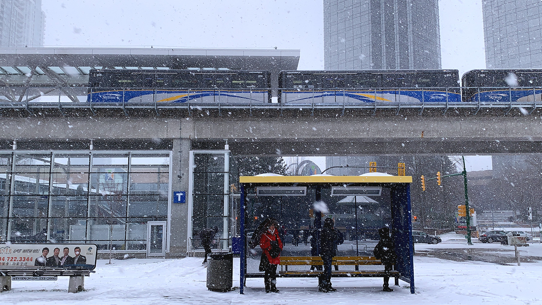 Commuters waiting at a bus stop while SkyTrain passes by at Metrotown Station