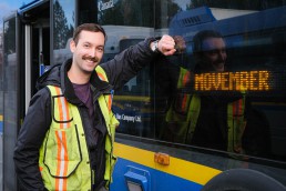 Photo of Stephen Wright standing in front of the Movember bus-stash double-decker bus