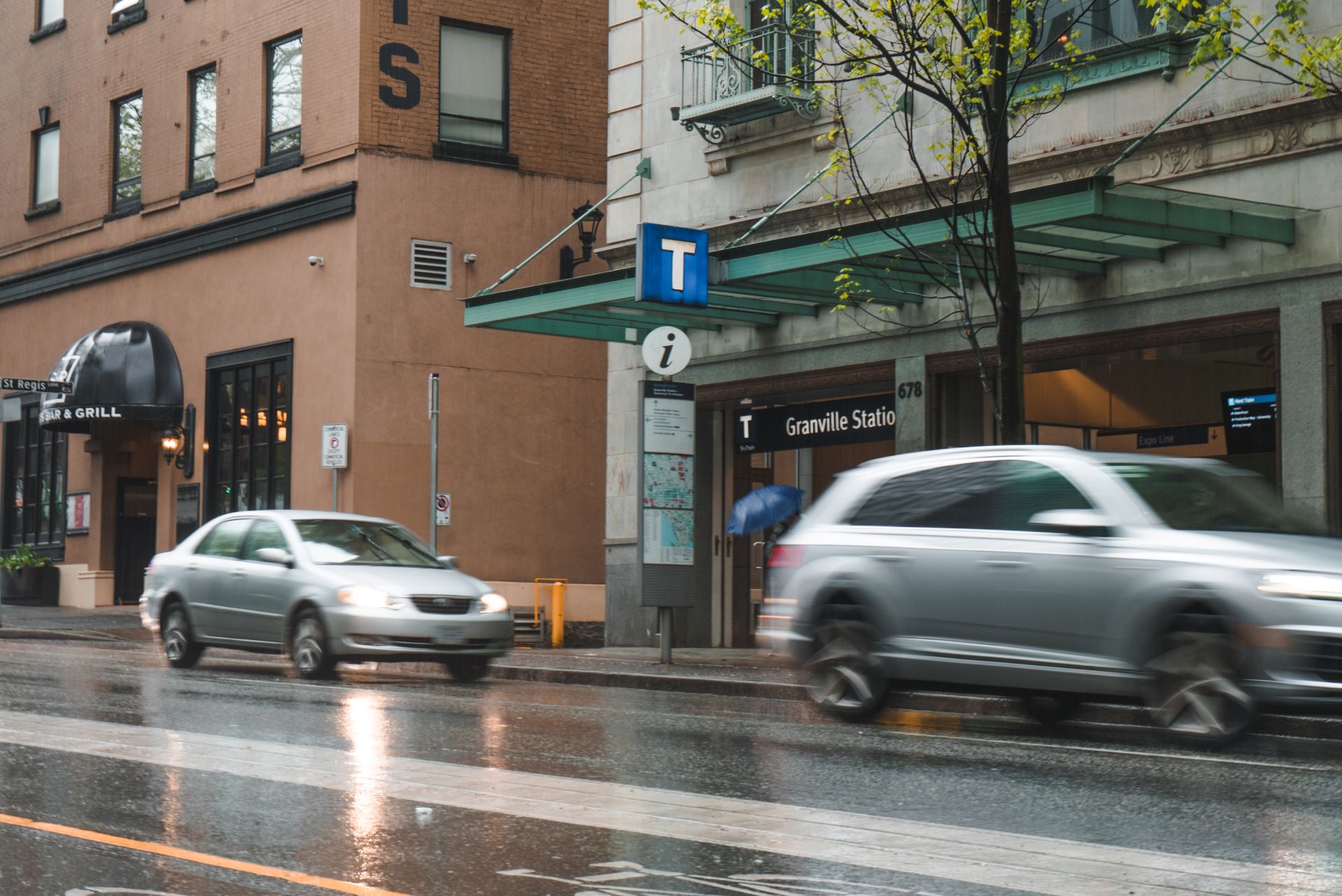 Cars drive past the Dunsmuir entrance of Granville Station on a rainy day