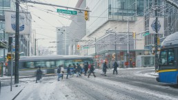 People cross Granville Street at Robson Street, past a bus, in downtown Vancouver on a snow day