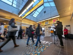 A poet reads poetry at Waterfront Station as people pass by