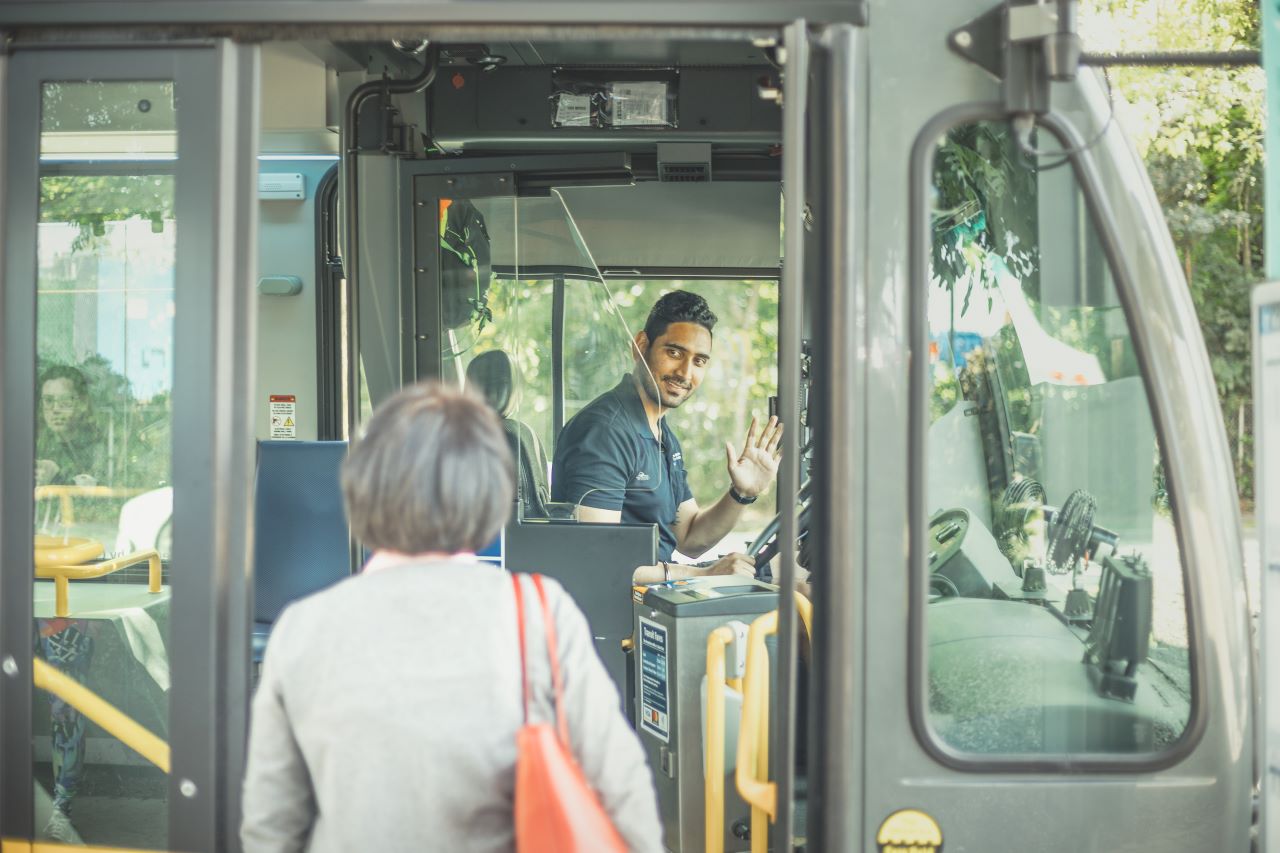 A bus operator waves to a customer as they board the bus