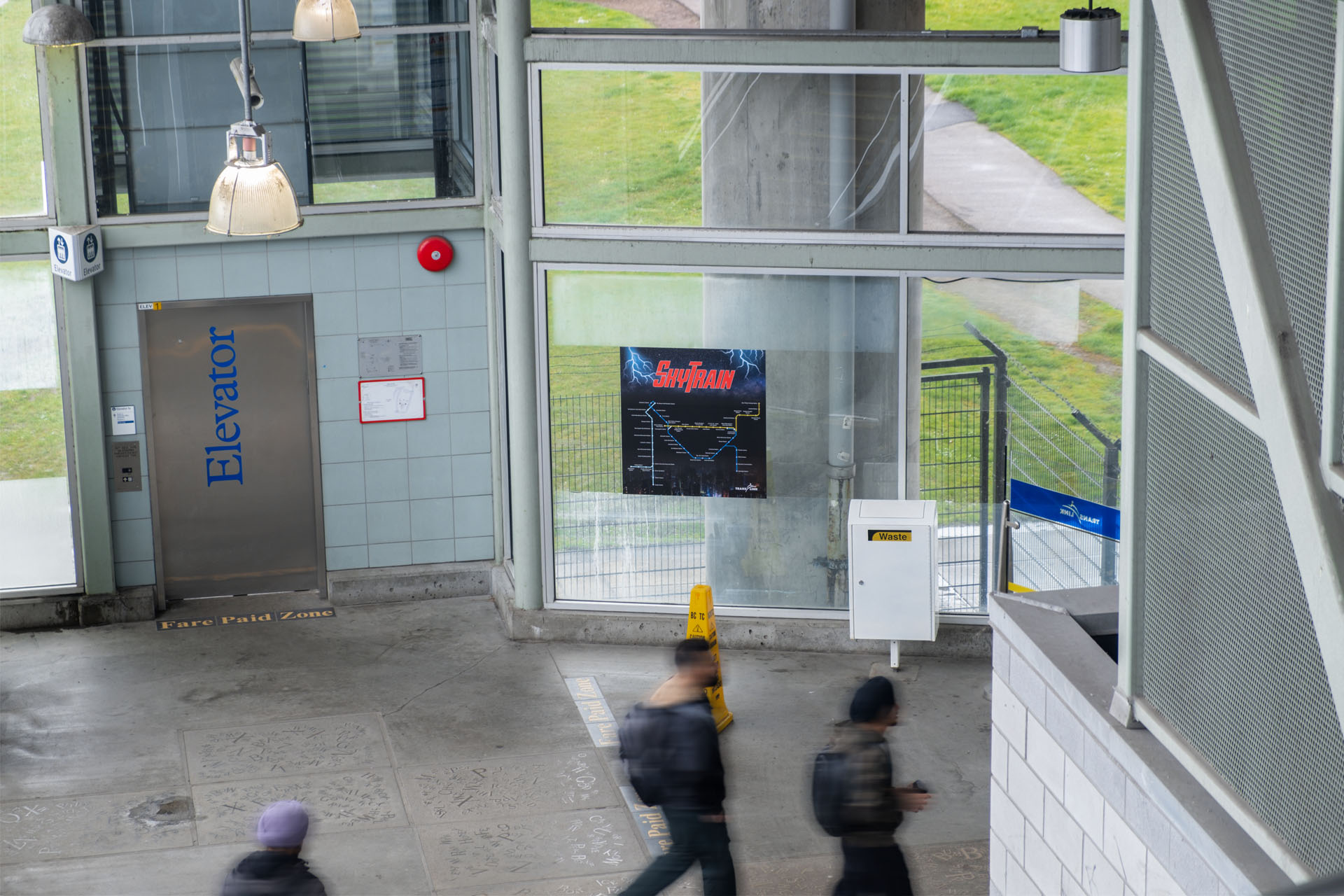 People walking by the Avengers SkyTrain map at Braid Station
