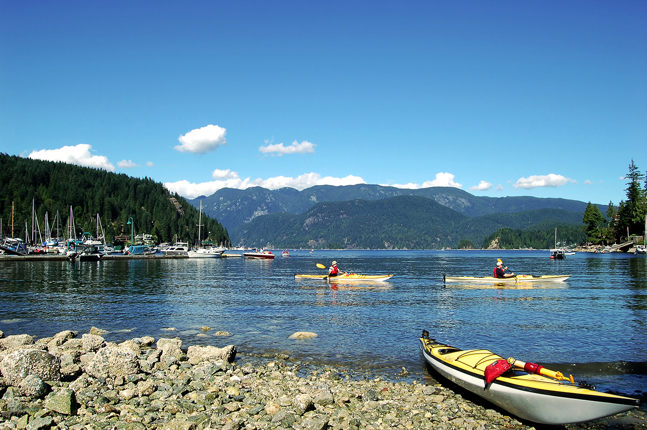 A kayak parked near the bay and two people kayaking at Deep Cove