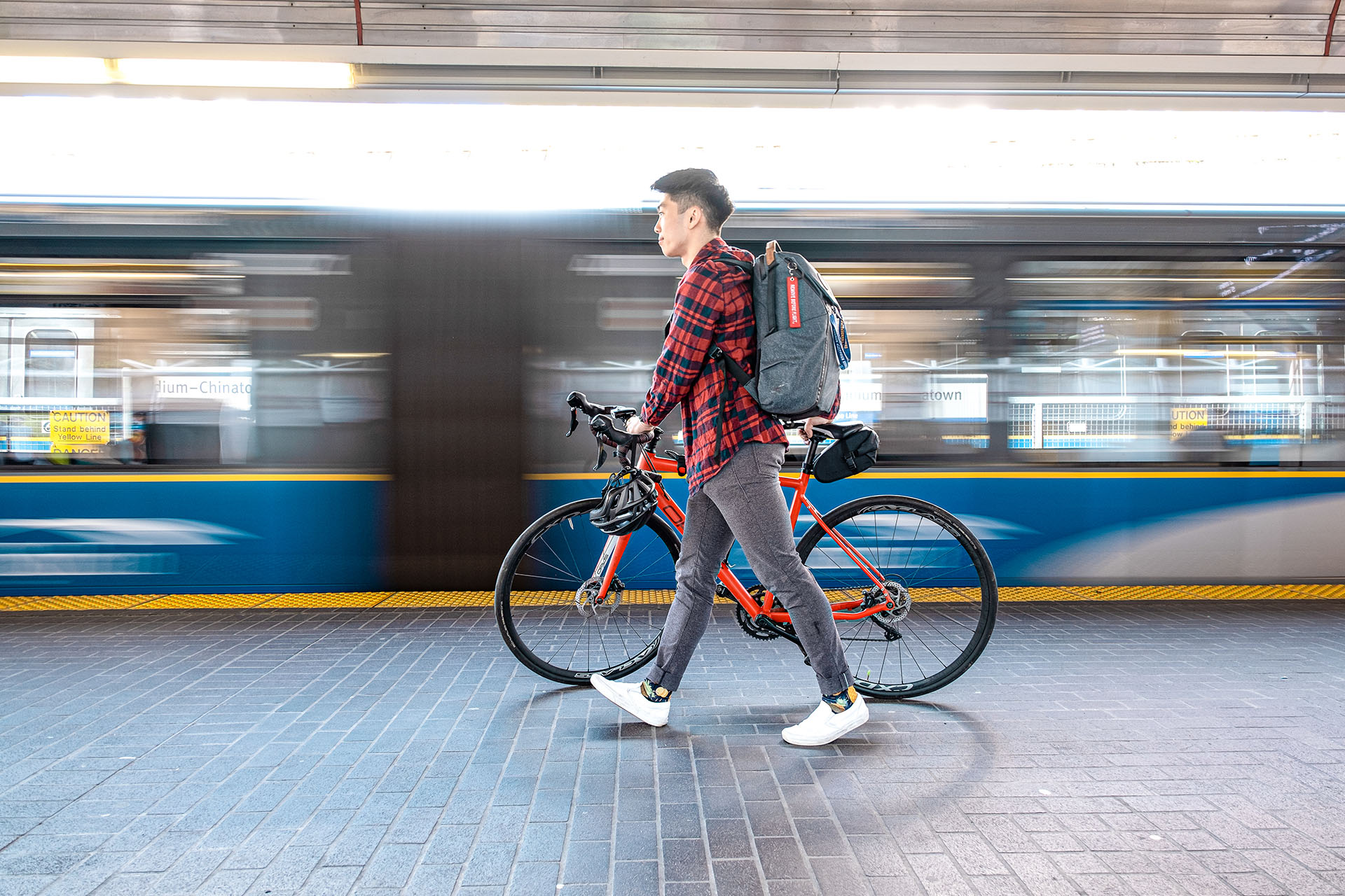 A person with a bike, walking alongside a SkyTrain at a SkyTrain station
