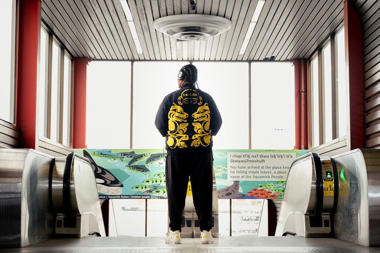 DJ O Show stands in front of art made by a Squamish Nation artist at Waterfront Station