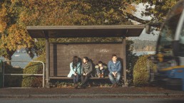 A family sitting at a bus shelter as bus arrives at the stop