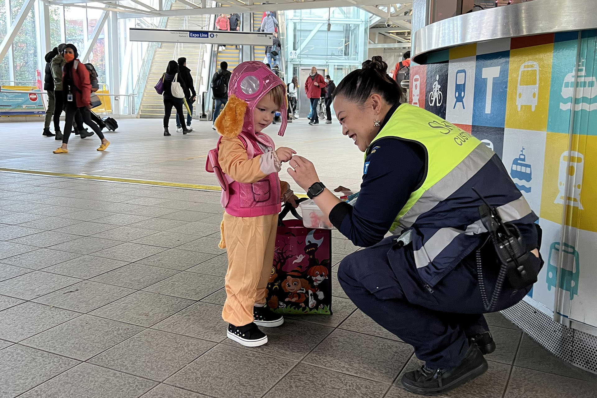 A SkyTrain Attendant, giving candy to a child in costume