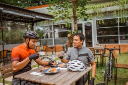 Two cyclists, sitting at a table, drinking water and coffee