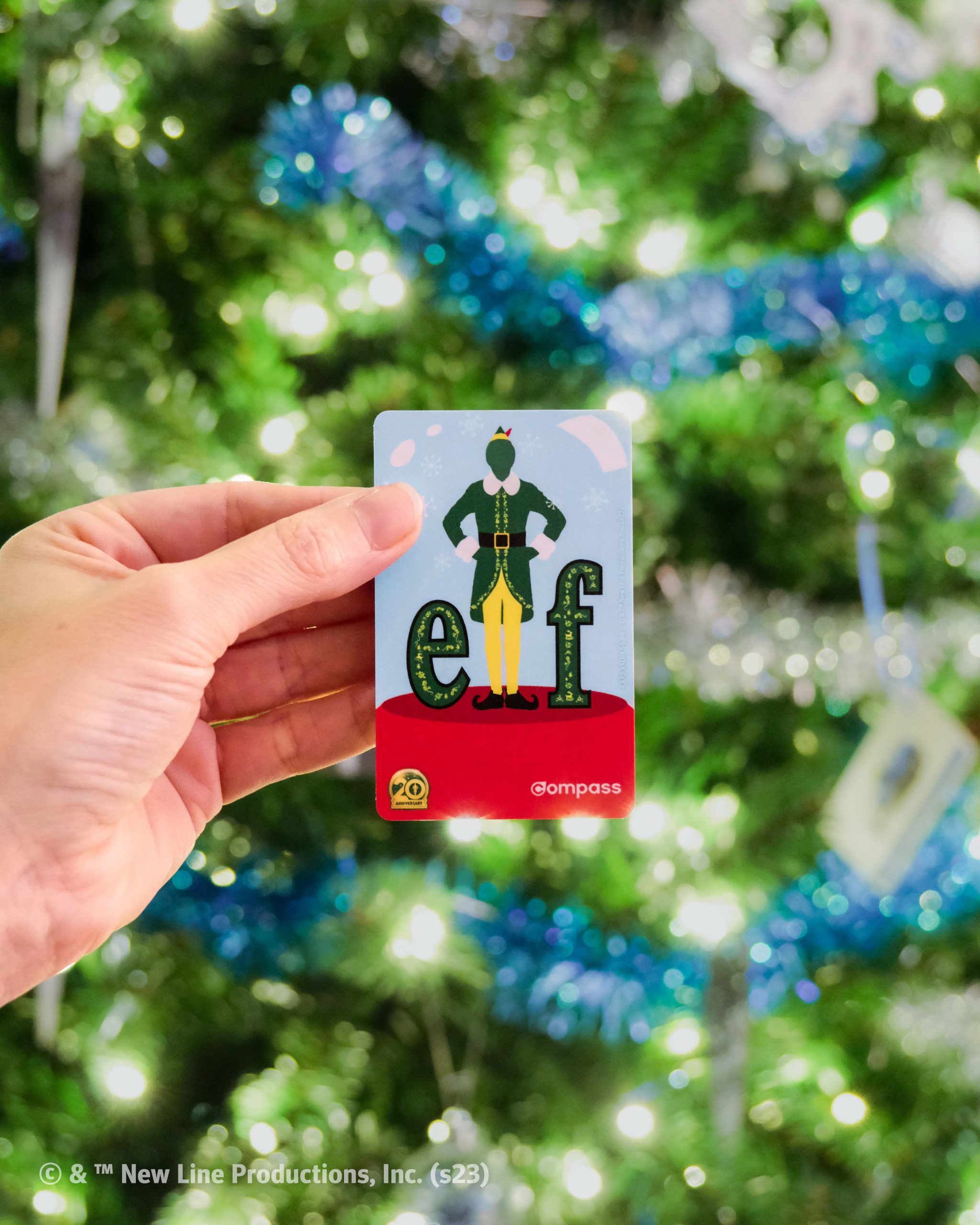 Photo of a Limited-edition Elf Compass Card being held up in front of a Christmas Tree