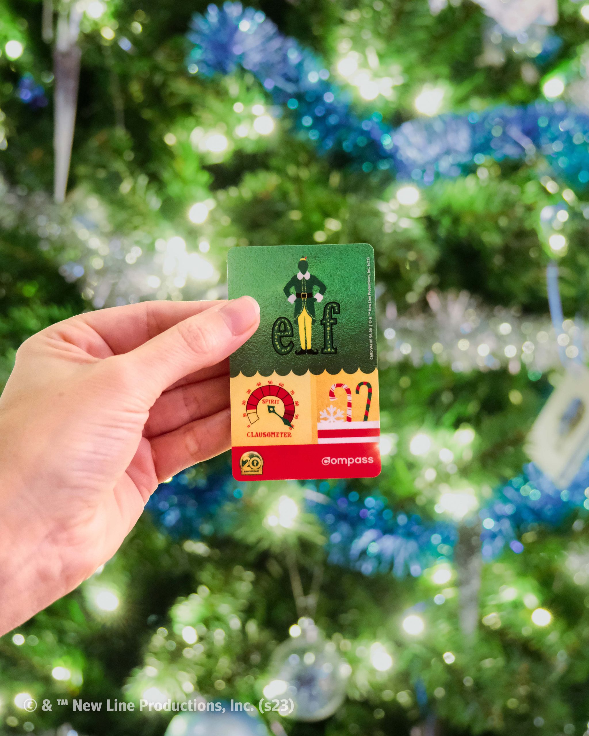 Photo of one Limited-edition Elf Compass Card being held up in front of a Christmas tree
