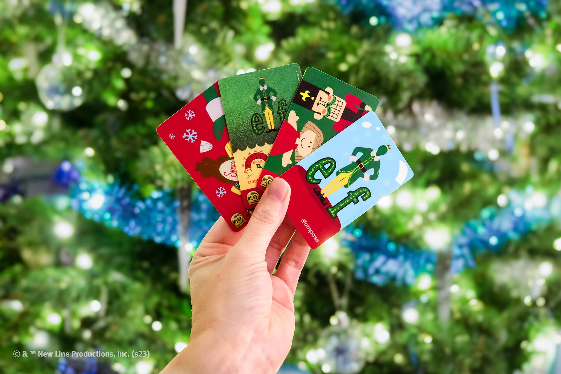 A collection of four Limited-edition Elf Compass Cards in front of a Christmas tree