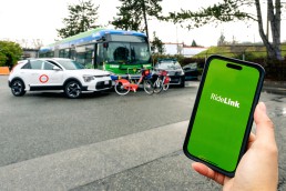 RideLink app on phone with Modo car, Evo car, Mobi bikes, and RapidBus in the background