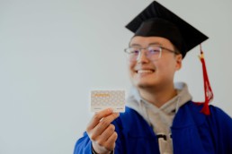 A person holding a GradPass while wearing a graduation cap and gown