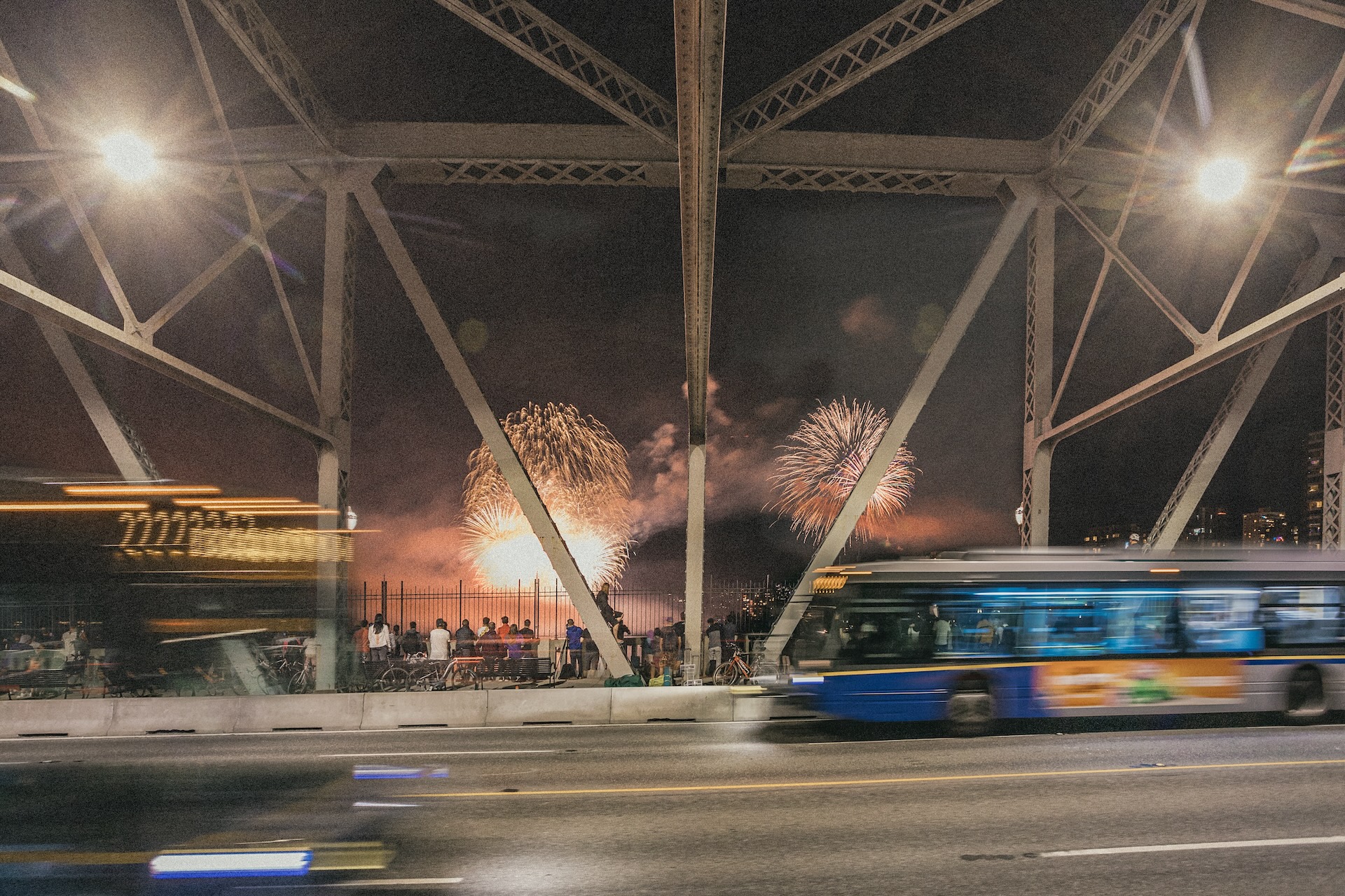 A bus driving on Burrard Street Bridge with the fireworks in the background