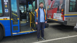 Bus operator Travis Noel standing outside the front door of a bus