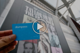 A person holding up a Compass Card at BC Place with a play button on the image