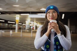 woman wears a new TransLink Store toque and matching scarf while drinking a coffee at Lonsdale Quay