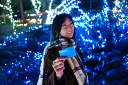 A person holding up a Compass Card in front of holiday lights