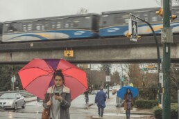 Person with an umbrella looking at phone with SkyTrain in background