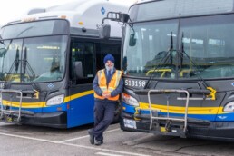 A man wearing a turban stands in between two large buses.