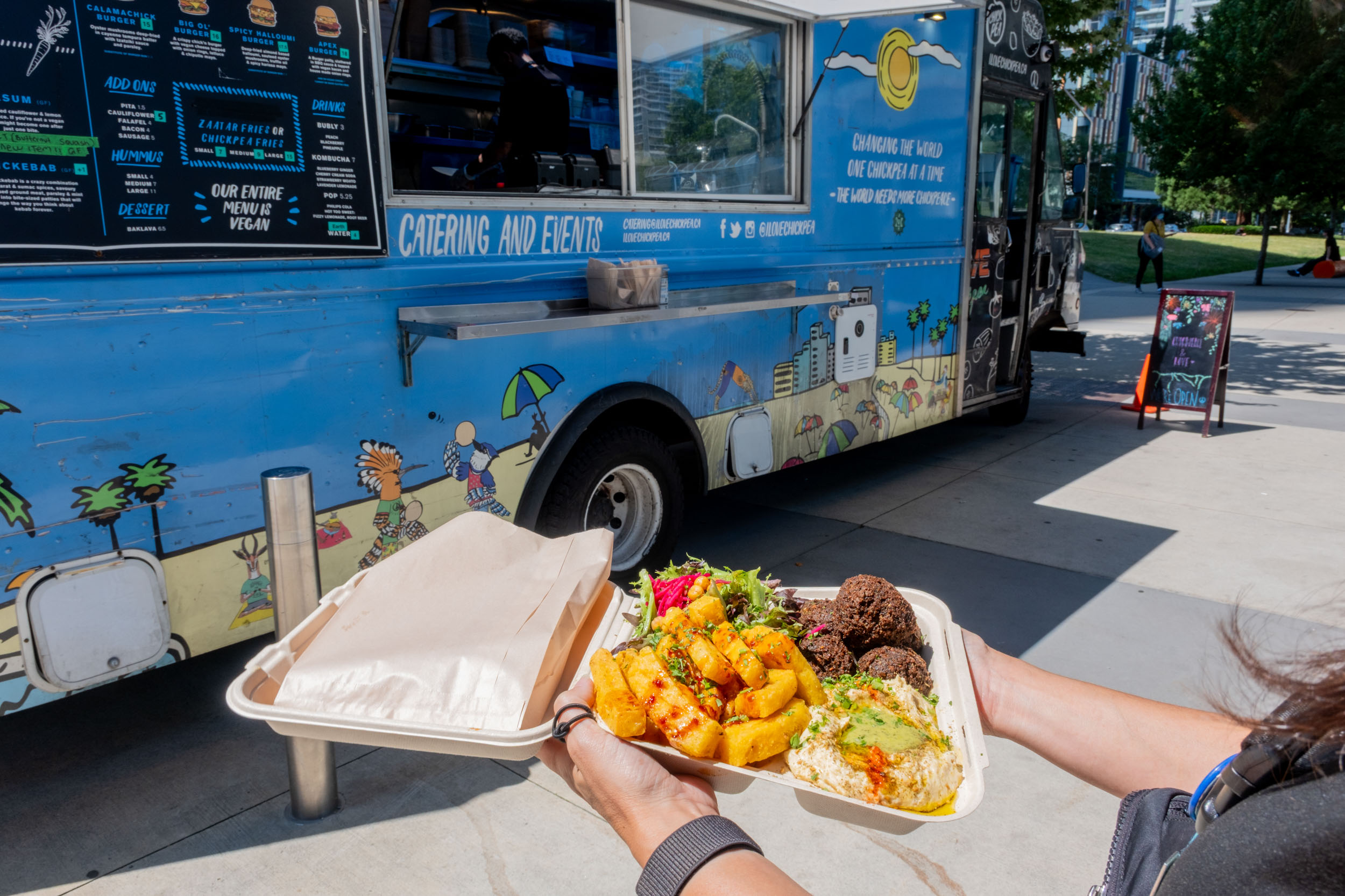 Customer holds a platter of food in a to-go container from the Chickpea food truck at Metrotown Station