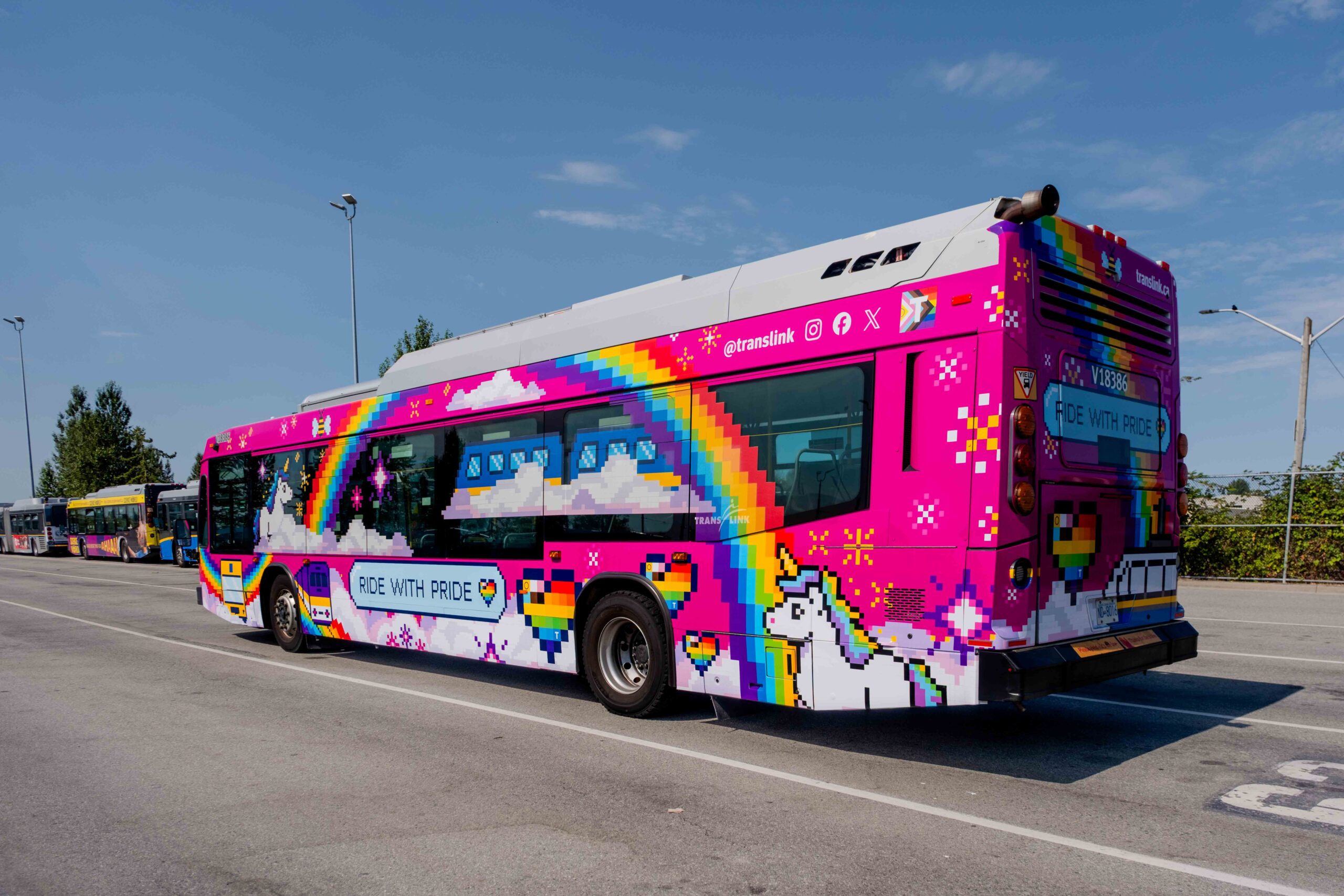 A colorful bus with pixel art of rainbows, unicorns, clouds, hearts, and stars on a pink background. The side of the bus displays the phrase 'RIDE WITH PRIDE' in blue letters on a white cloud.