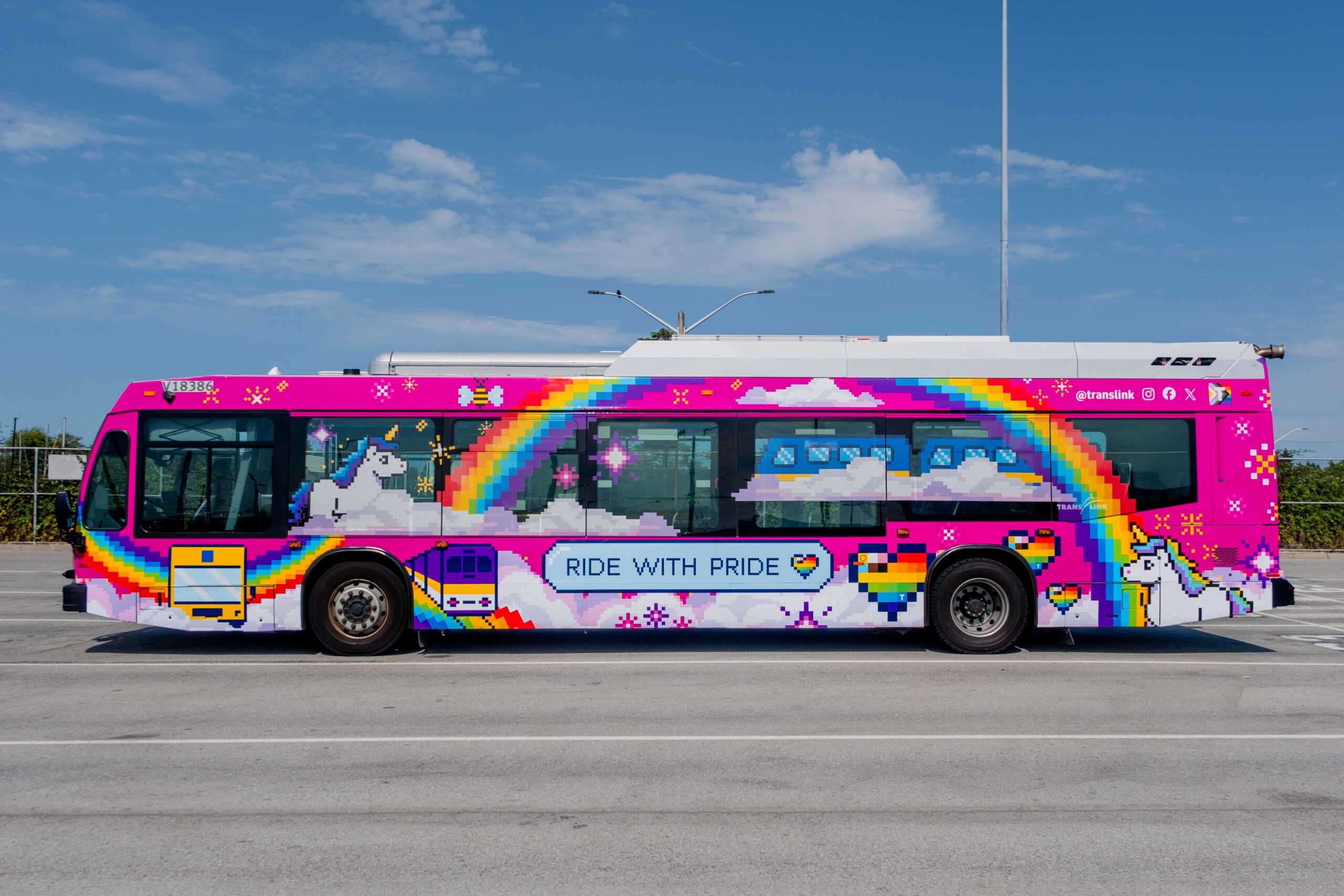 A colorful bus with pixel art of rainbows, unicorns, clouds, hearts, and stars on a pink background. The side of the bus displays the phrase 'RIDE WITH PRIDE' in blue letters on a white cloud.