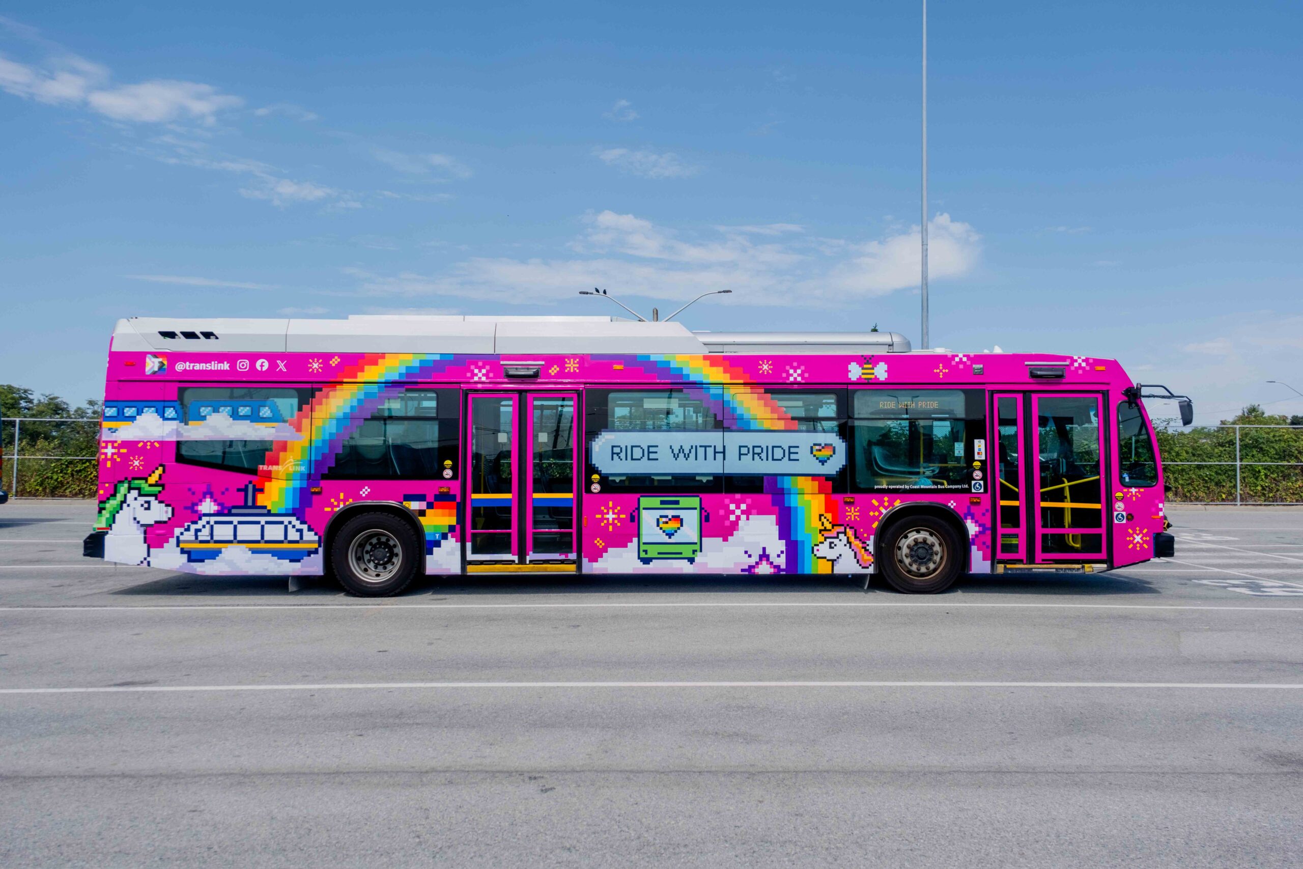 A colorful bus with pixel art of rainbows, unicorns, clouds, hearts, and stars on a pink background. The side of the bus displays the phrase 'RIDE WITH PRIDE' in blue letters on a white cloud.