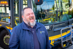 Bus operator Kelly Podlubny laughs at a bus stop with a bus parked in the background