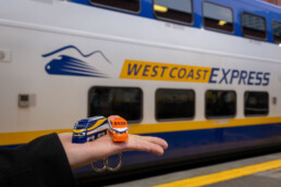 A person holds up the Compass Mini-WCE on their palm in front of a West Coast Express car